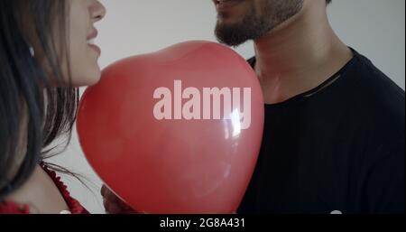 Una coppia che tiene tra di loro un palloncino rosso a forma di cuore Foto Stock