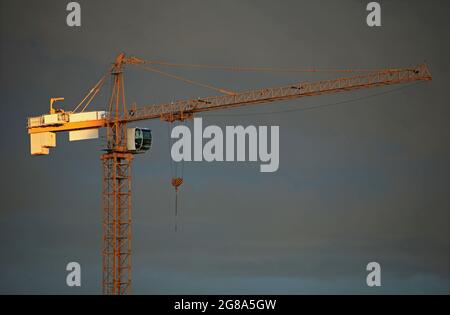 Singola gru di costruzione sullo sfondo grigio del cielo nei raggi del sole giallo della sera. Cantiere con gru Foto Stock