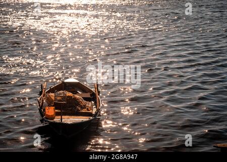 Piccola barca da pesca in mare in Grecia. Luce del mattino quasi alla luce del sole, raggio arancione sparso sul mare, con barca da pesca e frizzante surf in mare Foto Stock