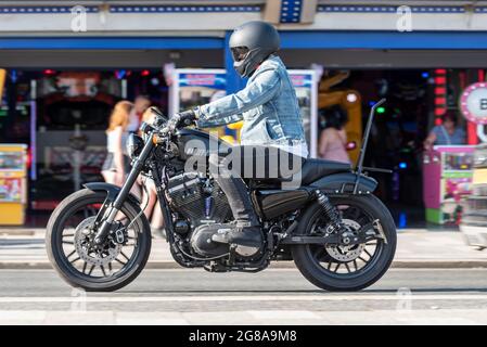 Il motociclista Harley Davidson corre lungo la Marine Parade a Southend on Sea, Essex, in una calda giornata estiva, passando davanti alla galleria di divertimenti, indossando denim Foto Stock