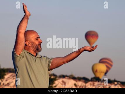 Cappadocia, Turchia. 18 luglio 2021. Un uomo si pone per una foto mentre i mongolfiera volano sopra la Cappadocia, Turchia, il 18 luglio 2021. Credit: Mustafa Kaya/Xinhua/Alamy Live News Foto Stock