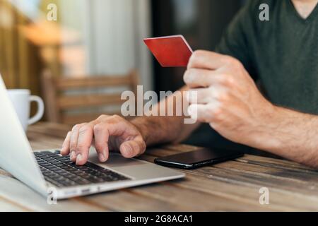 Shopping online dal balcone di casa, uomo che utilizza computer portatile, smartphone mobile e carta di credito per l'acquisto di articoli su Internet, fuoco selettivo Foto Stock