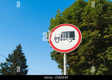 Segnale circolare rosso e bianco con cargo nero indicante che non è possibile accedere ai camion con alberi e cielo blu sullo sfondo Foto Stock