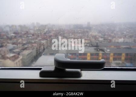 maniglia della finestra e gocce di pioggia sulla finestra di fronte al paesaggio urbano mentre piove all'esterno Foto Stock