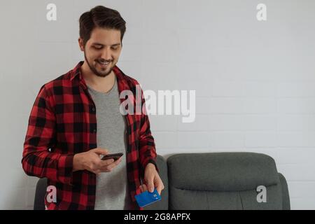 Uomo latino in camicia rossa plaid e barba facendo un acquisto online in interni. Foto Stock