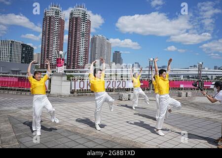 Tokio, Giappone. 19 luglio 2021. Un gruppo balla di fronte a un banner Tokyo 2020 mentre viene girato. Gli anelli si ergono su una zattera nella Baia di Tokyo di fronte al quartiere di Odaiba. Le Olimpiadi di Tokyo 2020 si terranno dal 23 luglio 2021 all'8 agosto 2021. Credit: Michael Kappeler/dpa/Alamy Live News Foto Stock