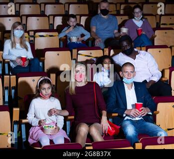 Persone in maschere protettive che guardano il film in modo assorbente al cinema Foto Stock