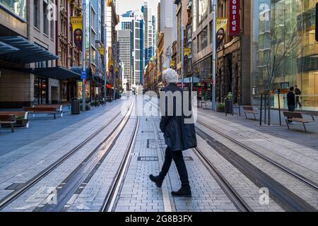 Uomo anziano con ritorno alla macchina fotografica che attraversa via vuota a Sydney, Australia CBD Foto Stock