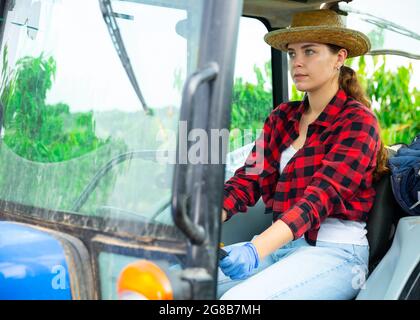 Giovane agricoltore specializzato che lavora su un trattore piccolo in frutteto Foto Stock