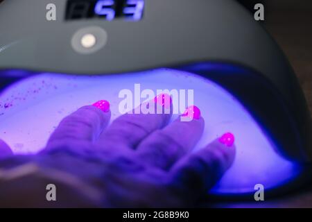 Donna mano all'interno lampada a LED UV per asciugare chiodi rosa con gel metodo, piastra di cura primo piano. Processo di manicure. Indurimento gel lucidante per unghie applicato di recente Foto Stock