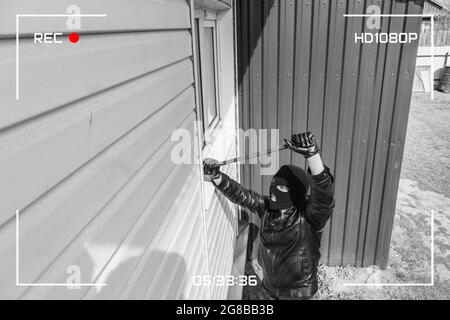 Vista CCTV del burglar che si rompe a casa attraverso la finestra con crowbar. Protezione di un edificio residenziale privato con l'aiuto di un video esterno Foto Stock