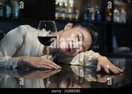 Una donna elegante si è addormentata al bar del ristorante dopo aver bevuto un paio di bicchieri di vino rosso Foto Stock