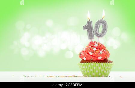 Compleanno cupcake con numero dieci candela bruciante su sfondo verde con spazio di copia per i vostri saluti Foto Stock