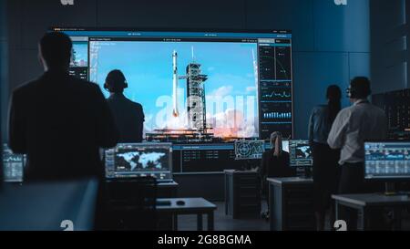 Gruppo di persone nel Mission Control Center testimoniano il successo del lancio di Space Rocket. I dipendenti del controllo di volo si trovano sui monitor e sugli schermi dei computer anteriori Foto Stock