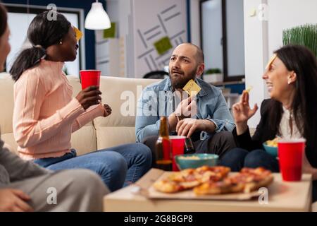 Una squadra diversificata di colleghi che giocano a incantati dopo il lavoro in ufficio. Gli amici multietnici si divertono a indovinare il gioco d'imiation come divertenti e allegri intrattenimenti con cibo e bevande Foto Stock