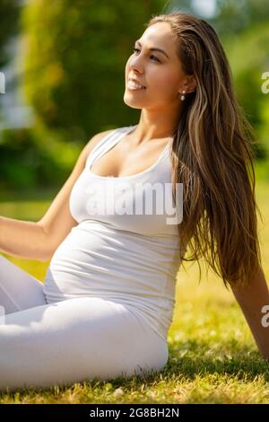 Felice incinta Donna seduta sul prato in un bel giardino Foto Stock