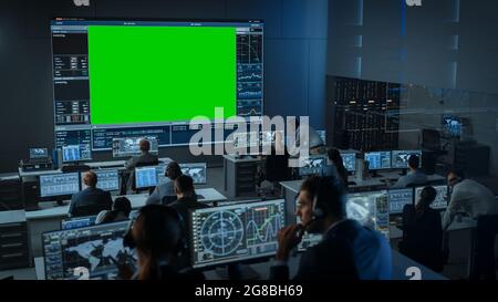 Big Green Screen Horizontal Mock Up in una sala Mission Control Center con Flight Director e altri Controllers che lavorano sui computer. Squadra di Foto Stock