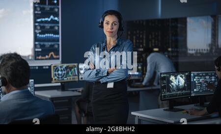 Ritratto di una bella Flight Controller femminile che posa per la fotocamera in un centro di controllo missione. Donna di successo che indossa una cuffia e la attraversa Foto Stock