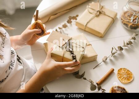 Mani che tengono elegante regalo di natale semplice in carta artigianale su tavola bianca. Concetto DIY Foto Stock