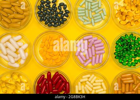 Assortiti vari tipi e molte misure di pillole farmaceutiche in vetro su sfondo giallo colorato in file. Foto Stock