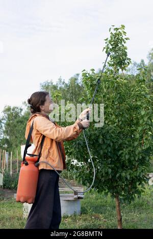 il lavoratore agricolo spruzza fungicidi e pesticidi in giardino per proteggere le piante dalle malattie e distruggere i parassiti Foto Stock