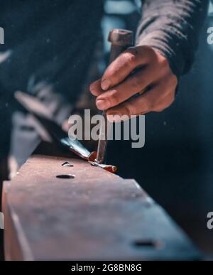 Primo piano delle mani di un fabbro durante la fucinatura artistica. Foto Stock