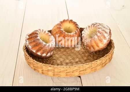 Tre dolci cupcake fatti in casa in un piatto di paglia, primo piano, su un tavolo di legno. Foto Stock