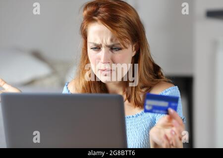 Donna confusa che acquista online con carta di credito e computer portatile a casa Foto Stock