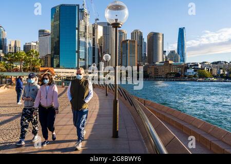 Escursionisti in maschere che si esercitano a Circular Quay, Sydney, Australia, durante il blocco pandemico. Cielo blu e skyline della città sullo sfondo Foto Stock