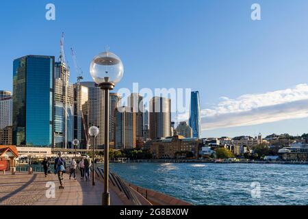 Escursionisti in maschere che si esercitano a Circular Quay, Sydney, Australia, durante il blocco pandemico. Cielo blu e skyline della città sullo sfondo Foto Stock