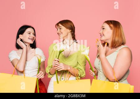Corpo amici positivi guardando donna con vitiligo e borsa per la spesa con fiore isolato su rosa Foto Stock