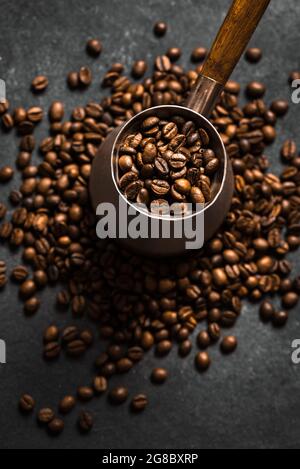 Caffè arrosto in grani e turk (cezve) su sfondo nero. Composizione di caffè turco, vista dall'alto, messa a fuoco selettiva. Foto Stock