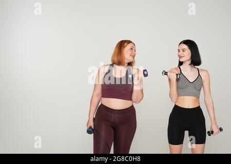 Corpo allegro sportivo positivo allenatore con manubri isolati su grigio Foto Stock