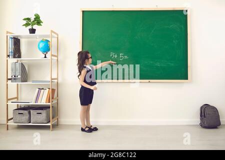 Ritorno a scuola. Vista posteriore di una studentessa in gesso scrive su una lavagna in classe. Foto Stock