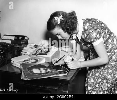 DEANNA DURBIN nel 1938 su set segni candidi / foto autografi per i suoi fan, mentre mangiando una mela pubblicità per Universal Pictures Foto Stock