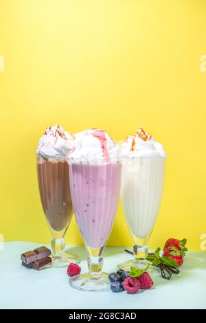 Bevande rinfrescanti estive, frullati, frullati pazzi con gelato, frutti di bosco, vaniglia, cioccolato. Su uno sfondo giallo blu brillante Foto Stock