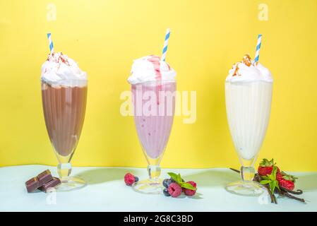 Bevande rinfrescanti estive, frullati, frullati pazzi con gelato, frutti di bosco, vaniglia, cioccolato. Su uno sfondo giallo blu brillante Foto Stock