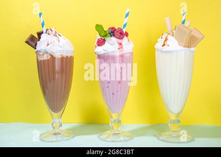 Bevande rinfrescanti estive, frullati, frullati pazzi con gelato, frutti di bosco, vaniglia, cioccolato. Su uno sfondo giallo blu brillante Foto Stock