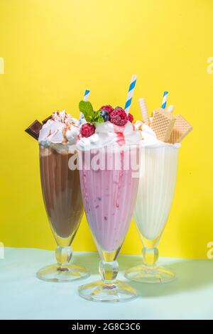 Bevande rinfrescanti estive, frullati, frullati pazzi con gelato, frutti di bosco, vaniglia, cioccolato. Su uno sfondo giallo blu brillante Foto Stock