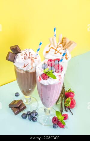 Bevande rinfrescanti estive, frullati, frullati pazzi con gelato, frutti di bosco, vaniglia, cioccolato. Su uno sfondo giallo blu brillante Foto Stock