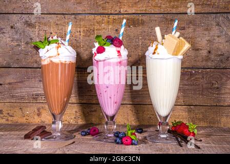 Bevande rinfrescanti estive, frullati, frullati pazzi con gelato, frutti di bosco, vaniglia, cioccolato. Su sfondo classico in legno Foto Stock