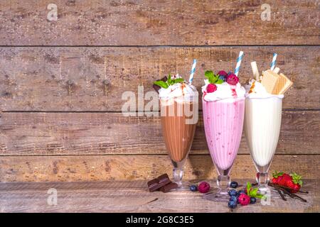 Bevande rinfrescanti estive, frullati, frullati pazzi con gelato, frutti di bosco, vaniglia, cioccolato. Su sfondo classico in legno Foto Stock