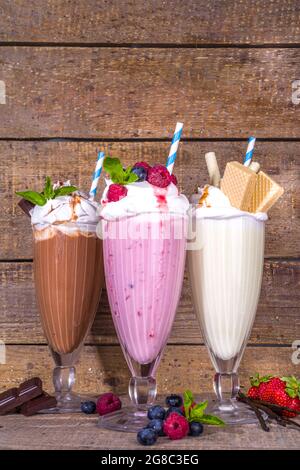 Bevande rinfrescanti estive, frullati, frullati pazzi con gelato, frutti di bosco, vaniglia, cioccolato. Su sfondo classico in legno Foto Stock