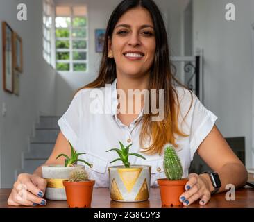 donna che guarda la macchina fotografica con succulenti in vaso in casa. Foto Stock