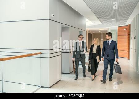 Gruppo di colleghi che escono dall'ascensore, si comunicano mentre si cammina attraverso il corridoio Foto Stock