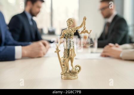 Primo piano della figura della giustizia in piedi sul tavolo con un gruppo di avvocati che si riuniscono in background Foto Stock