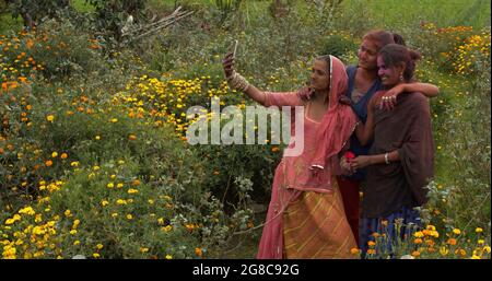 Le femmine indiane che prendono un selfie sullo sfondo di fiori mentre partecipano al festival Holi Foto Stock