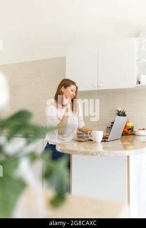 Ritratto di una ragazza bellissima e sorridente che usa un computer portatile sul posto di lavoro. Scuotendo la mano per dire Ciao qualcuno dal suo laptop. Incontri online o soggiorno Foto Stock