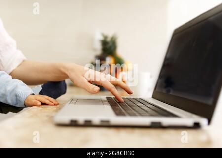 Madre che lavora su un computer portatile con un bambino. Vista laterale delle mani di donna e bambino sul notebook. Mamma e bambino di affari che usano il computer portatile in casa. Da a. Foto Stock