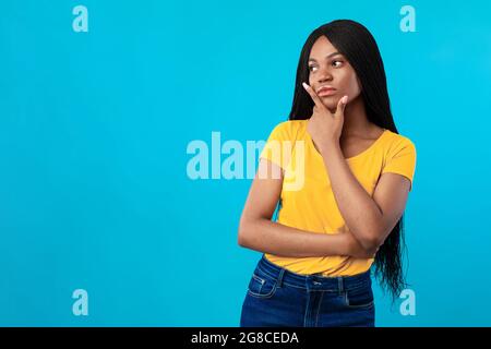 African American Lady Thinking in piedi vicino spazio vuoto, sfondo blu Foto Stock